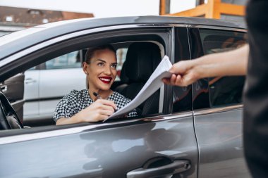 Yeni arabasında oturan tatmin olmuş ve gülümseyen bayan alıcı. İkinci el araba satıcısıyla alıcı sözleşmesi imzalarken mutlu oluyor.