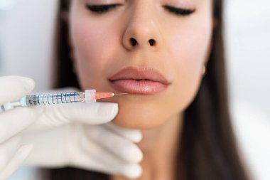 Çekici kadın güzellik kliniğinde gençleştirici yüz enjeksiyonu yaptırıyor. Güzellik uzmanı kadın kırışıklıklarını botulinyum toksin iğneleriyle ya da hyaluronik asit doldurucularıyla dolduruyor..