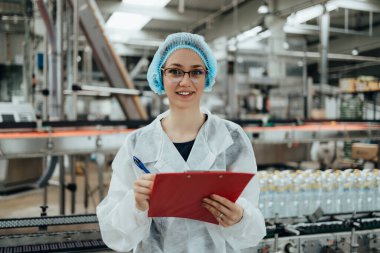 Female worker in protective workwear working in medical supplies research and production factory and checking canisters of distilled water before shipment. Inspection quality control.  clipart