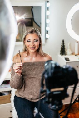 Evden ya da atölyeden güzel makyaj videosu yayınlayan mutlu genç bir kadın. Güzel çevrimiçi içerik kozmetikçisi makyaj yapıyor ve bazı iş araçlarını açıklıyor. Günlük kaydı ve çevrimiçi kanal çalışması. 