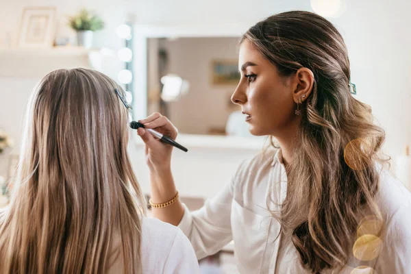 近照一张漂亮的年轻女子的脸正在化装 这位艺术家正在用刷子刷眼影 专业美容师工作 — 图库照片