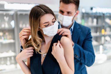 Yüz koruyucu maskeli güzel bir çift modern kuyumcudan alışveriş yapıyor. Genç bayan, harika bir kolye ve küpe deneyin. Moda tarzı ve zarafet konsepti. Salgın yaşam tarzı.