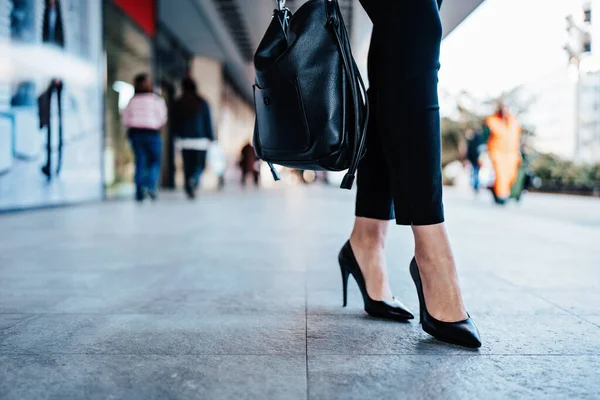 Close up shot of business woman\'s legs in black shoes standing on city street. Plenty of defocused empty space in background for text or decoration. Shallow depth of field.