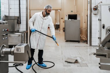 Orta yaşlı erkek, endüstriyel mezbahada çalışıyor ve günlük işini bitiriyor. Gıda işleme tesisi zeminini ve makine üretim hatlarını suyla temizliyor ve yıkıyor..