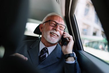 Lüks arabada arka koltukta oturan yakışıklı kıdemli iş adamı. Akıllı telefonunu kullanıyor ve duygusal tepki veriyor. Kurumsal iş anlayışında taşımacılık.