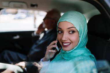 Üst düzey iş adamı ile birlikte lüks arabada arka koltukta oturan hijab ile güzel Müslüman Arap kadın. Dizüstü bilgisayarını kullanıyor..