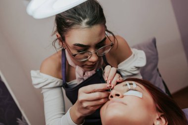 Kirpik uzatma prosedüründeki güzel kızıl saçlı kadın. Kozmetik ve vücut bakımı yakın çekim. Sığ alan derinliği ve seçici odak.