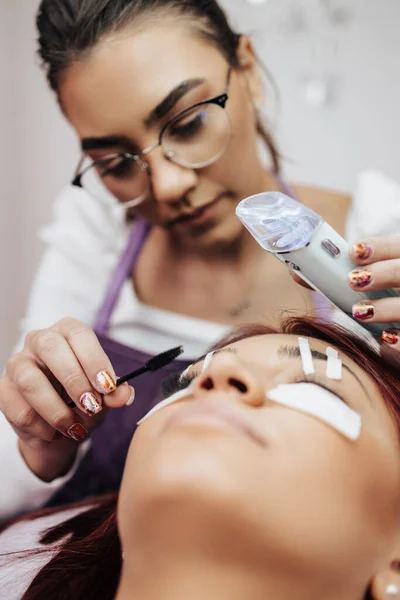 Beautiful young redhead  woman at eyelash extension procedure. Cosmetics and body care close up shot. Shallow depth of field and selective focus.