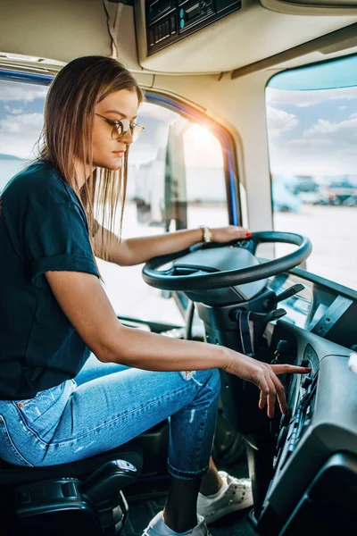 Portrait of beautiful young woman professional truck driver sitting and driving big truck. Inside of vehicle. People and transportation concept.