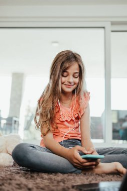 Beautiful girl lies on the floor of the living room of her house and uses a laptop and smart phone for learning and communication. She is happy and smiled.