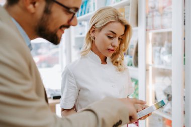 Young business man choosing and buying drugs in a drugstore while talking with attractive female pharmacist. She helping him with expert advice.