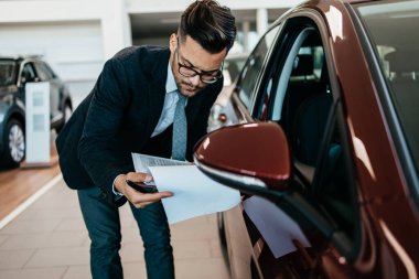 Galeride çalışan araba satıcısı ve araba detaylarını son kez kontrol ediyor alıcı gelmeden önce..