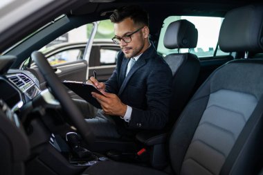 Galeride çalışan araba satıcısı ve araba detaylarını son kez kontrol ediyor alıcı gelmeden önce..