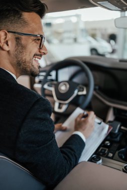 Galeride çalışan araba satıcısı ve araba detaylarını son kez kontrol ediyor alıcı gelmeden önce..