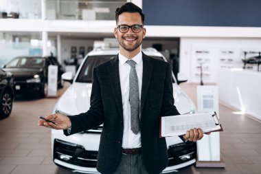 İyi görünümlü, neşeli ve samimi satıcı bir araba salonu veya showroom pozlar.