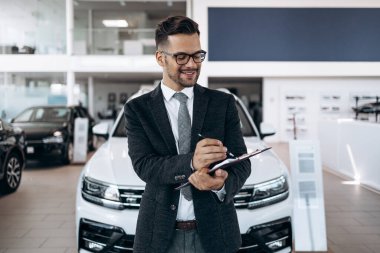 İyi görünümlü, neşeli ve samimi satıcı bir araba salonu veya showroom pozlar.