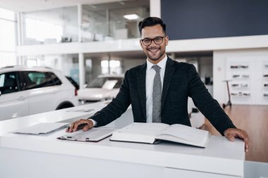 İyi görünümlü, neşeli ve samimi satıcı bir araba salonu veya showroom pozlar.