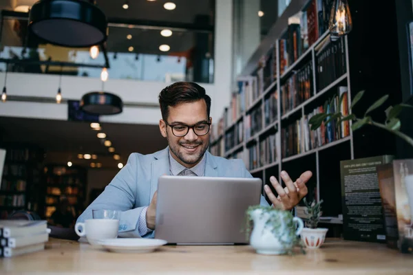Genç yakışıklı adam modern kitapçıda oturuyor, dizüstü bilgisayarını veya bilgisayarını okuyor ve kullanıyor..