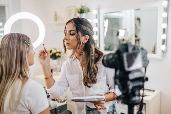 Evden ya da atölyeden güzel makyaj videosu yayınlayan mutlu genç bir kadın. Güzel çevrimiçi içerik kozmetikçisi makyaj yapıyor ve bazı iş araçlarını açıklıyor. Günlük kaydı ve çevrimiçi kanal çalışması. 