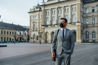 Handsome middle age businessman standing on city street. He is wearing face protective mask as protection during Coronavirus pandemic.