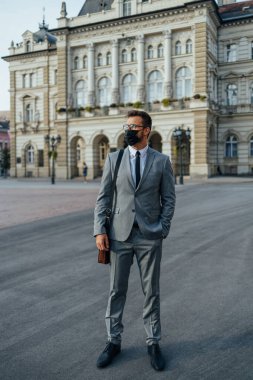 Handsome middle age businessman standing on city street. He is wearing face protective mask as protection during Coronavirus pandemic.