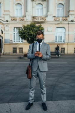 Handsome middle age businessman using smart phone on city street. People communication technology and lifestyle during virus pandemic concept. 