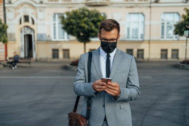 Handsome middle age businessman using smart phone on city street. People communication technology and lifestyle during virus pandemic concept. 