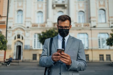 Handsome middle age businessman using smart phone on city street. People communication technology and lifestyle during virus pandemic concept. 