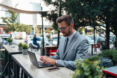 Orta yaşlı işadamı kafeteryada oturuyor ve iki toplantı arasında kahve molası veriyor. Dizüstü bilgisayar kullanıyor ve pozitif ve kendinden emin..