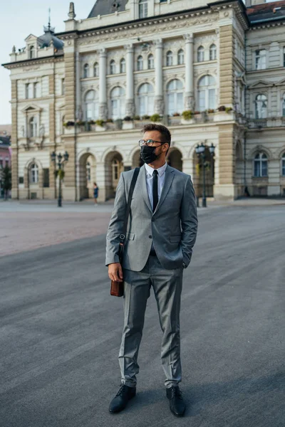 Handsome middle age businessman standing on city street. He is wearing face protective mask as protection during Coronavirus pandemic.