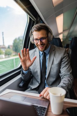 Yakışıklı iş adamı yüksek hızlı trenle seyahat ederken iyi vakit geçiriyor. Çevrimiçi iletişim, oyun ve eğlence için dizüstü bilgisayar ve kablosuz kulaklık kullanıyor.
