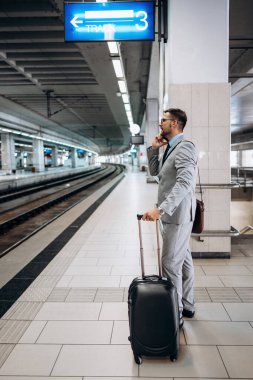 Bavullu yakışıklı orta yaşlı işadamı istasyon peronunda duruyor ve hızlı tren ya da metro bekliyor. Modern ve hızlı seyahat kavramı.