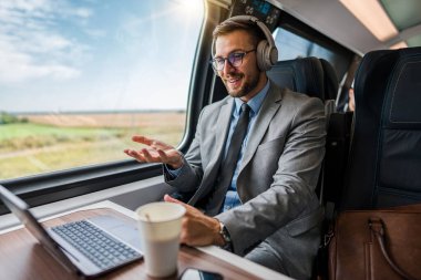 Yakışıklı iş adamı yüksek hızlı trenle seyahat ederken iyi vakit geçiriyor. Çevrimiçi iletişim, oyun ve eğlence için dizüstü bilgisayar ve kablosuz kulaklık kullanıyor.