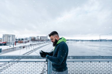 Çok soğuk ve karlı bir günde sakallı, koşan ve dışarıda egzersiz yapan yakışıklı orta yaşlı bir adam. Spor ve spor motivasyon teması. Aktivite verilerini takip etmek için akıllı telefon kullanıyor..