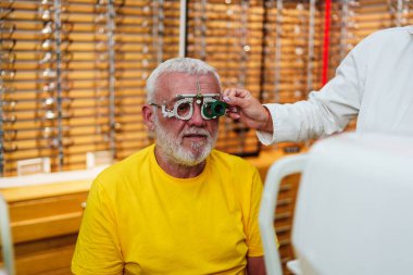 Positive senior male patient checking vision at modern ophthalmology clinic with optical trial frames.