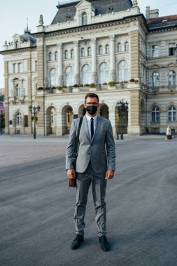 Handsome middle age businessman standing on city street. He is wearing face protective mask as protection during Coronavirus pandemic.