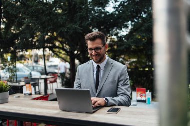 Orta yaşlı işadamı kafeteryada oturuyor ve iki toplantı arasında kahve molası veriyor. Dizüstü bilgisayar kullanıyor ve pozitif ve kendinden emin..