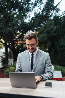 Orta yaşlı işadamı kafeteryada oturuyor ve iki toplantı arasında kahve molası veriyor. Dizüstü bilgisayar kullanıyor ve pozitif ve kendinden emin..