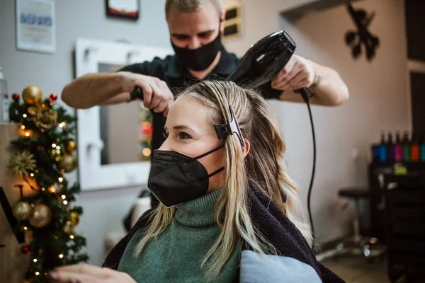 Beautiful hairstyle of woman after dyeing hair and making highlights in hair salon. She is wearing protective face mask as protection against virus pandemic.