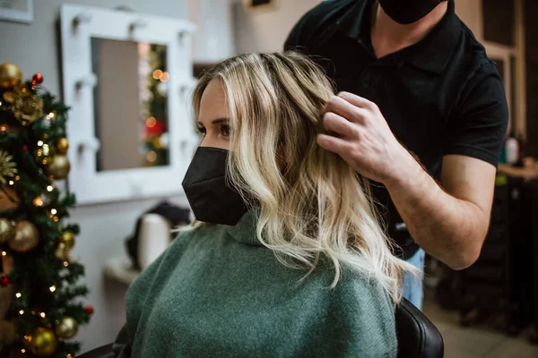 Beautiful hairstyle of woman after dyeing hair and making highlights in hair salon. She is wearing protective face mask as protection against virus pandemic.