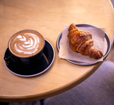 A mug of latte coffee with Croissant coffee break on wooden table