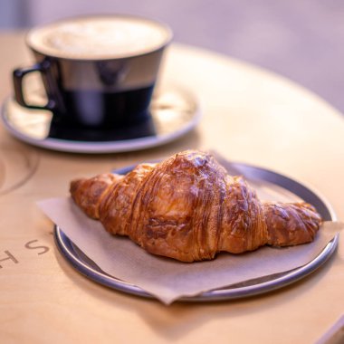 A mug of latte coffee with Croissant coffee break on wooden table