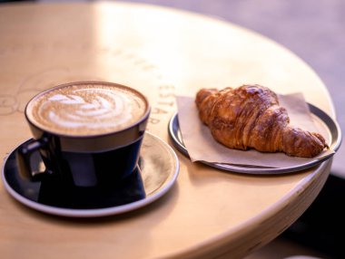 A mug of latte coffee with Croissant coffee break on wooden table
