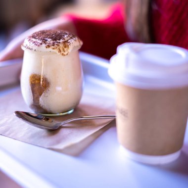 Woman holding tray with take away coffee and Tiramisu in glass