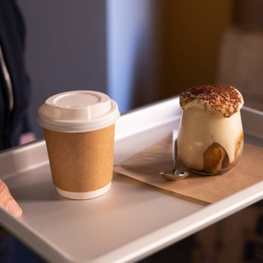Man holding tray with take away coffee and Tiramisu in glass. coffee flavored Italian dessert made of ladyfingers and mascarpone