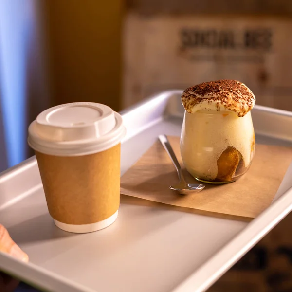 Man holding tray with take away coffee and Tiramisu in glass. coffee flavored Italian dessert made of ladyfingers and mascarpone