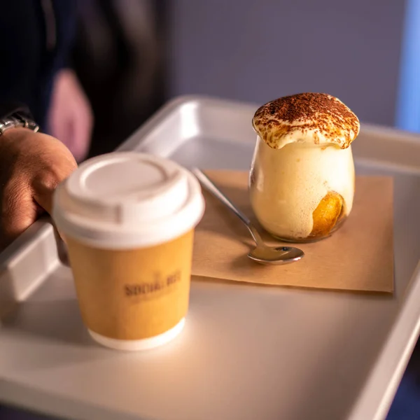 Man holding tray with take away coffee and Tiramisu in glass. coffee flavored Italian dessert made of ladyfingers and mascarpone