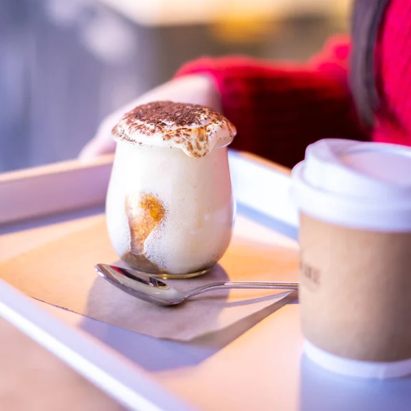 Woman holding tray with take away coffee and Tiramisu in glass