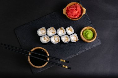 Macro shot of hosomaki sushi with soy sauce on natural black slate plate background with selective focus. Sushi with salmon and avocado