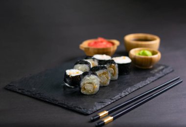 Macro shot of hosomaki sushi with soy sauce on natural black slate plate background with selective focus. Sushi with salmon and avocado